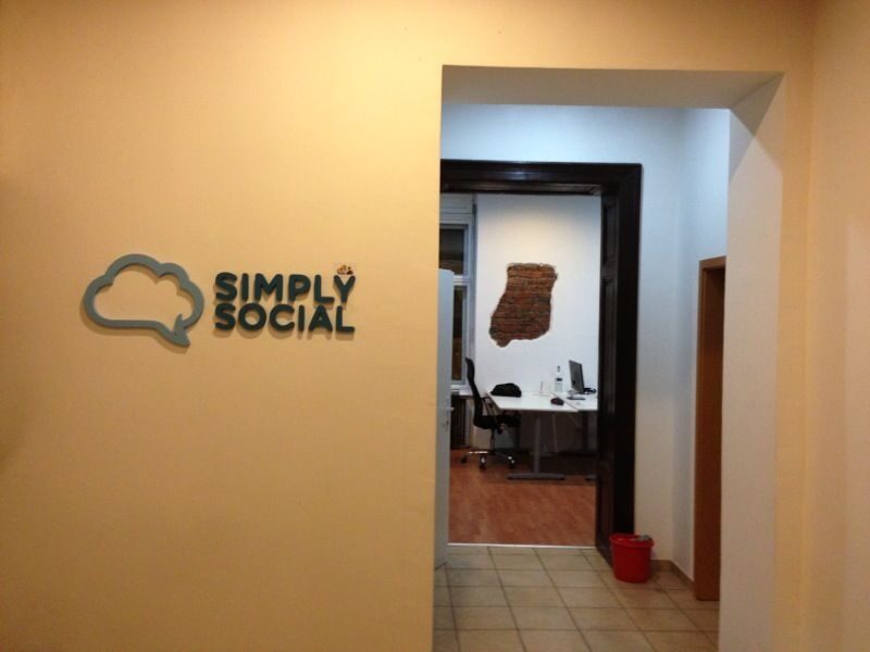 The SimplySocial office entrance, with the cloud-logo on the wall and a brick map of Romania visible through the doorway.