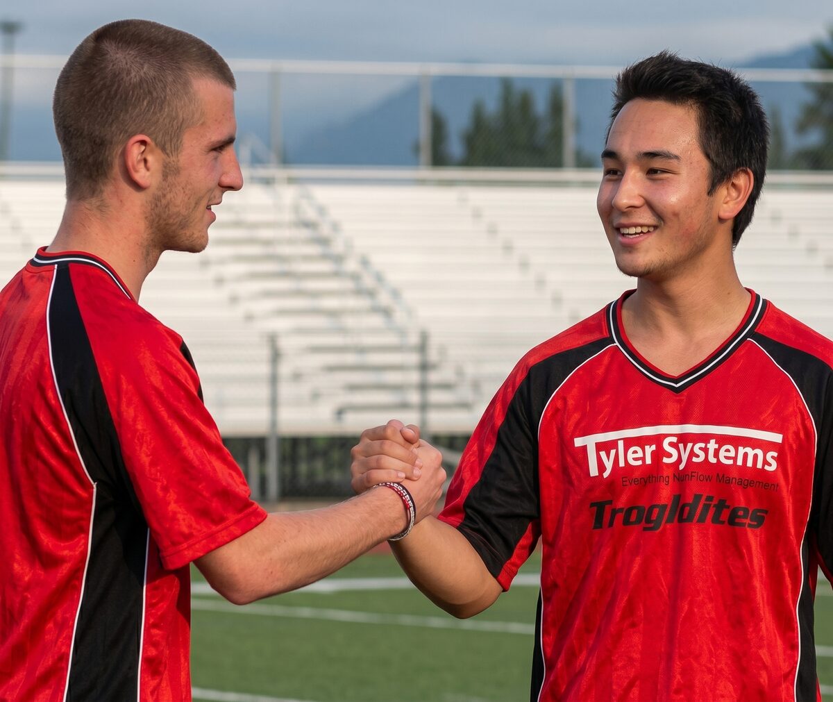 Two Tyler Systems / Troglodytes soccer players in red-and-black jerseys greeting each other on the field.
